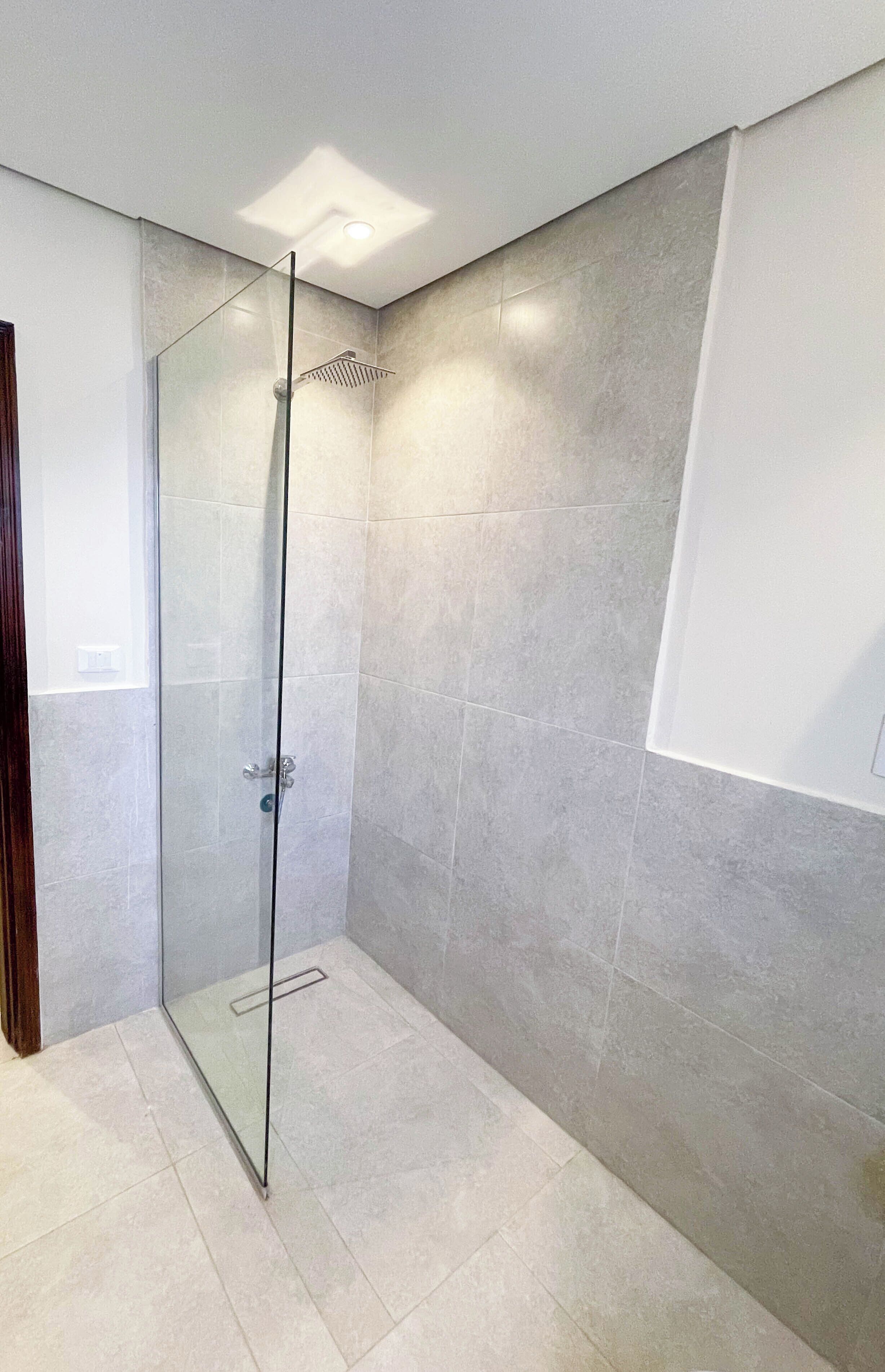A modern bathroom with a glass shower enclosure, tiled walls, and a recessed ceiling light.