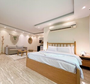A modern bedroom with a wooden bed, a sofa, a small table, and a wall-mounted air conditioner. - Settle Inn Aswar Apartments (New Cairo)