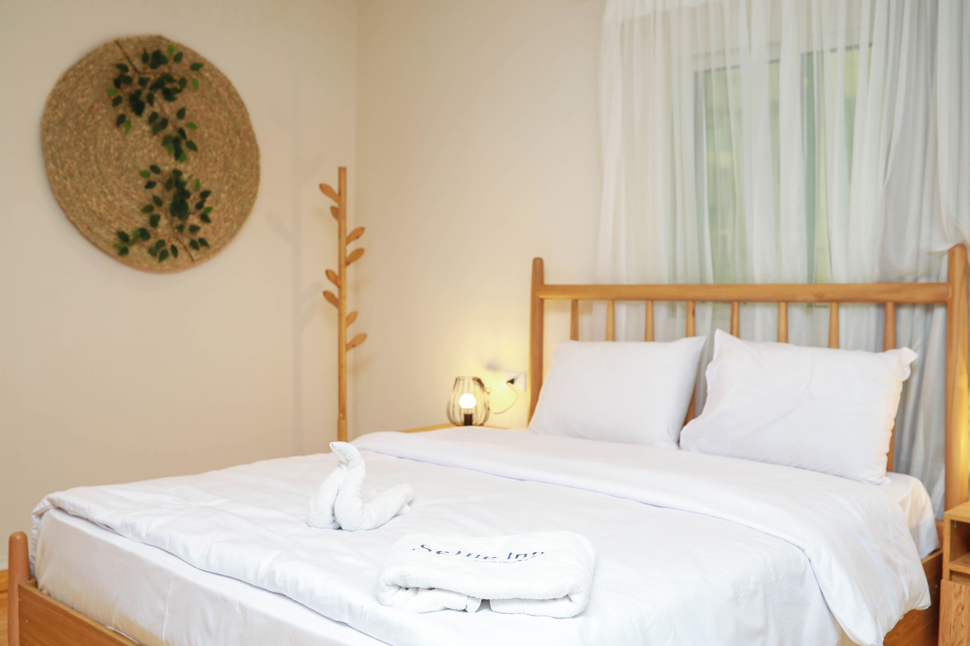 A neatly made bed with white linens, a wooden headboard, and a decorative wall hanging.