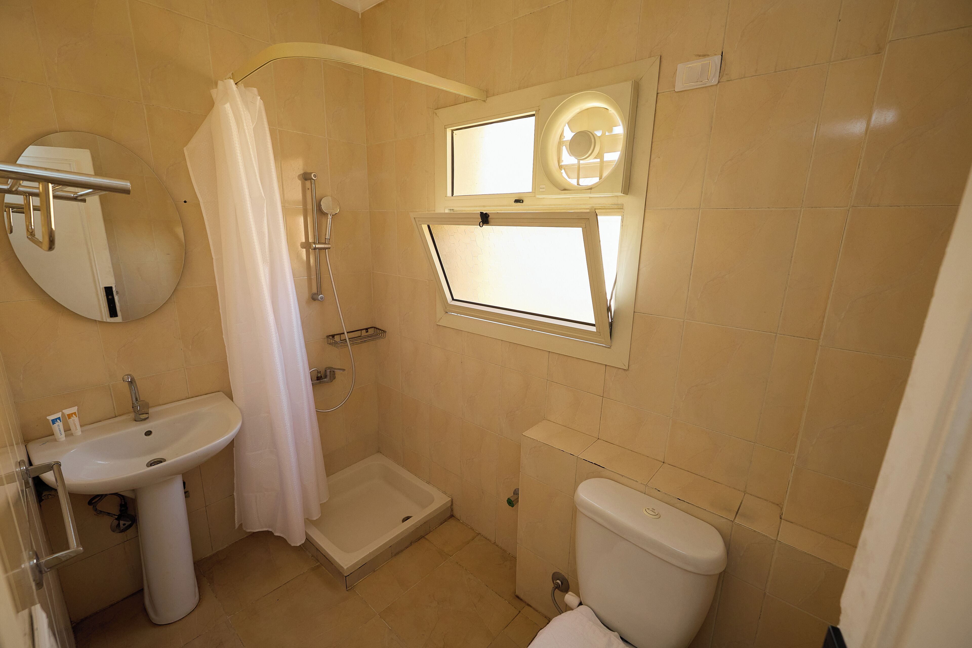 A bathroom with a sink, toilet, shower, and a window with a circular skylight.