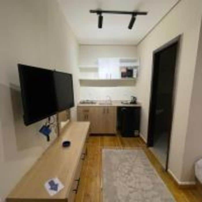 Passadís estret amb un televisor de pantalla plana fixat a la paret esquerra, una banca de fusta i una zona de cuina al fons.