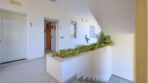 Un couloir avec une porte blanche, une porte en bois et un escalier menant à l’étage supérieur.