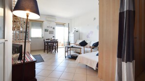 Une pièce bien éclairée comprenant un coin repas, un canapé et un lit. On y trouve une lampe, une table et un réfrigérateur.