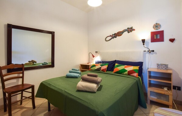 A bedroom with a bed, a chair, a nightstand, a lamp, and a wall clock.