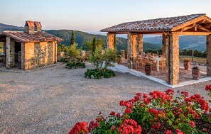 A rustic outdoor dining area with stone structures and a gravel ground, surrounded by greenery and flowers. - Cozy home in Trevinano (Trevinano)