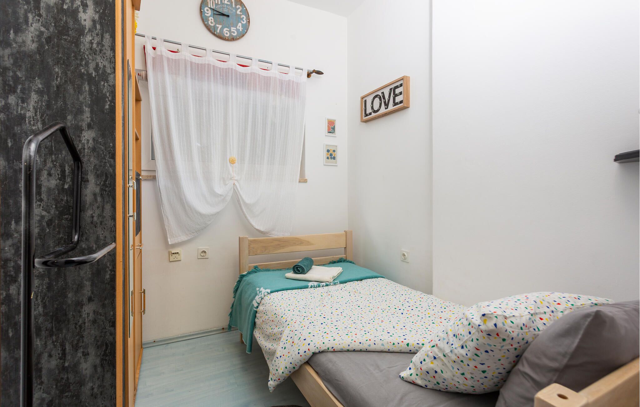 A bedroom with a bed, a clock, a 'LOVE' sign, and a curtain.