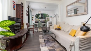 A modern living room with a sofa, coffee table, and TV. There is a kitchen in the background with a green archway. - 2 bedroom awesome apartment in Drazice (Drazice)