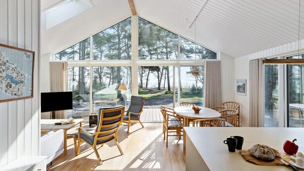 A spacious room with large windows, a dining area, and a kitchen.