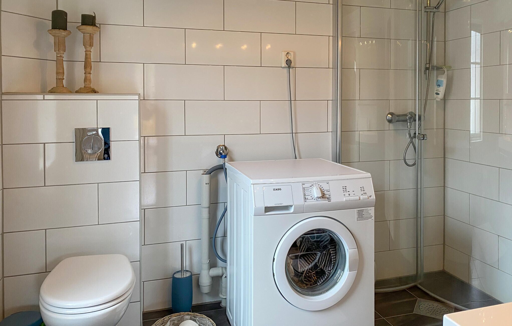 Ein modernes Badezimmer mit weiß gefliesten Wänden, einer weißen Waschmaschine, einer Toilette und einer Duschkabine.