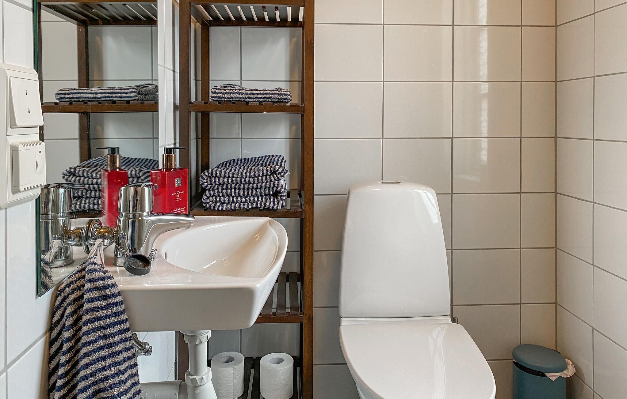 Een badkamer met een wit wastafel, een toilet en een plank met opgevouwen handdoeken.