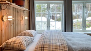 A room with a bed, two pillows, and a window with a view of trees and snow.