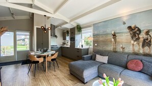 A modern living room with a grey sofa, wooden dining table, and a painting of children at the beach. - Awesome home in Andijk with WiFi (Andijk)