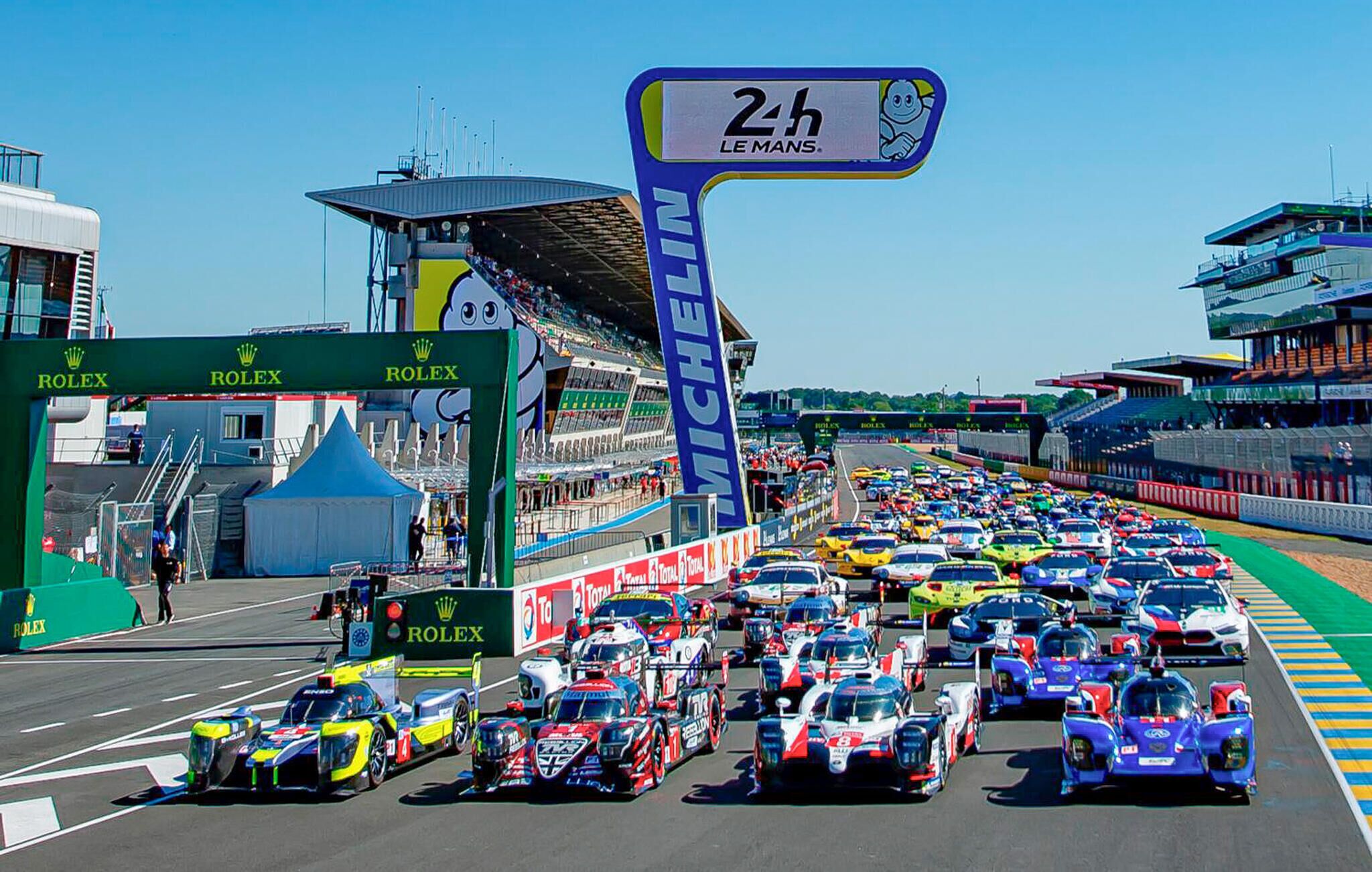 A busy race track with multiple racing cars and a large sign indicating '2h Le Mans'.