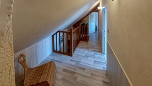 Un pasillo con piso de madera, una escalera con barandilla de madera y un banco tejido.