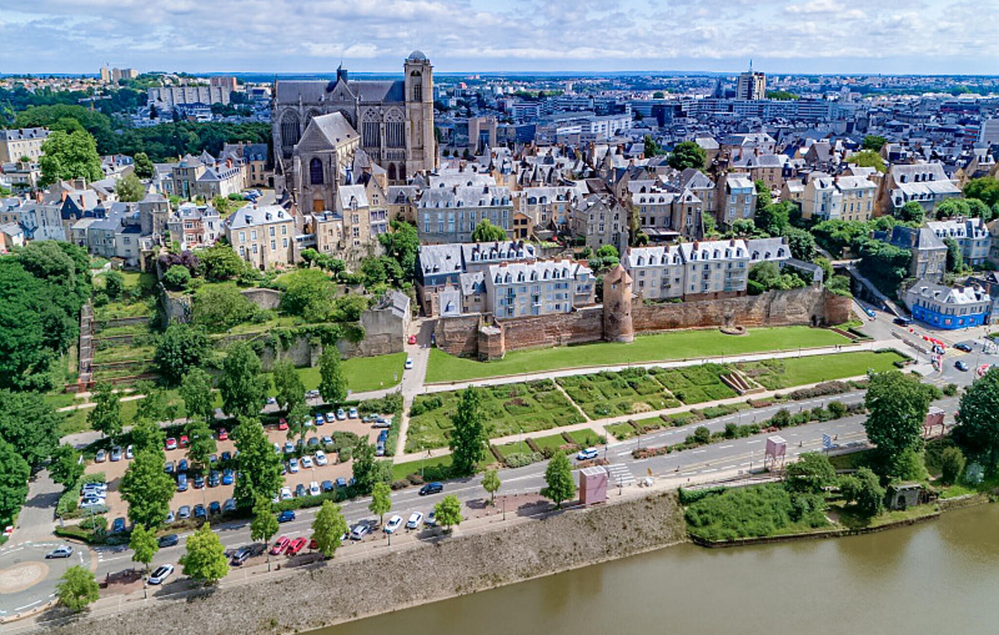 An aerial view of a historic city with a prominent cathedral, a fortified wall, and a river.
