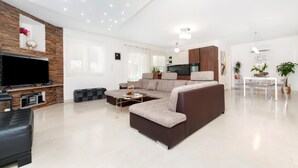 A modern living room with a sectional sofa, a flat-screen TV, a fireplace, and a dining area with clear chairs. - Gorgeous home in Rovinj (Rovinj)
