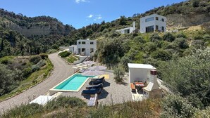 Una villa moderna con piscina, mobiliario de exterior y vistas a las colinas circundantes.