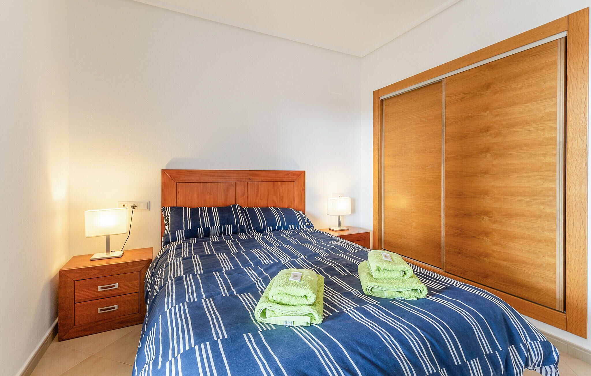 Une chambre à coucher avec un lit, deux tables de chevet, une armoire en bois et deux serviettes vertes sur le lit.