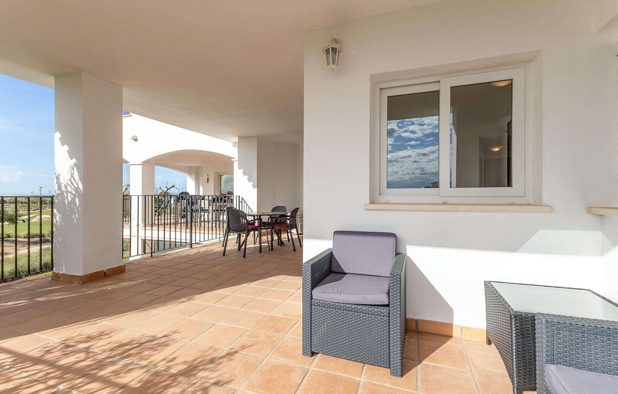 A covered patio with outdoor furniture, a view of a golf course, and a window with a view of the sky.