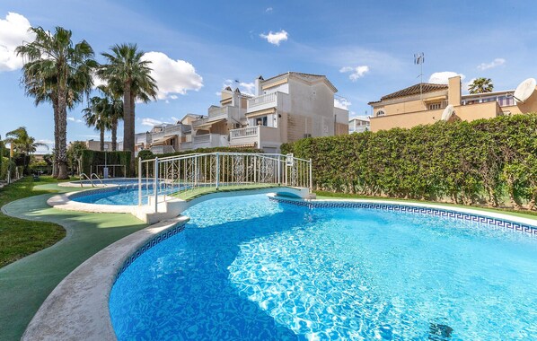 A swimming pool with a geometric tile pattern, surrounded by a white metal fence, palm trees, and a hedge. - Lovely home in Guardamar del segura (Guardamar del segura)