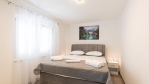 A bedroom with a bed, a nightstand, a lamp, a window with sheer curtains, and a painting of a mountain landscape. - Awesome home in Blato na Cetini (Blato na Cetini)