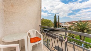 Ein Balkon mit einem weißen Plastikstuhl und einem Kissen, mit Blick auf ein Wohngebiet mit Häusern und Grünflächen.