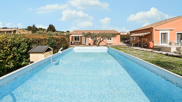 A swimming pool with a clear blue water surface, surrounded by a garden and a building with a tiled roof. - Comfortable, pittoresques (Combas)