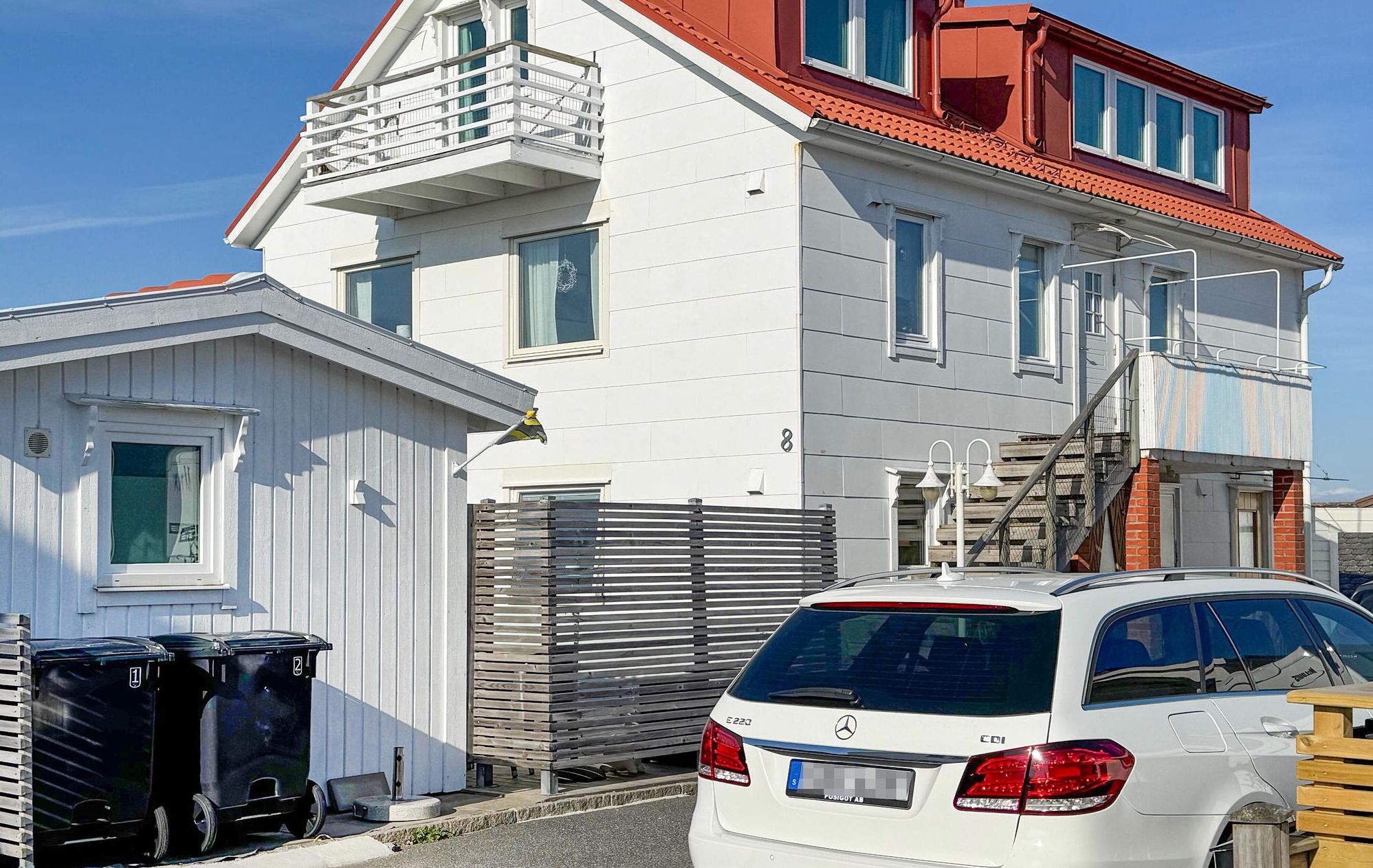 Een wit huis met twee verdiepingen, een rood dak, een balkon en een auto ervoor geparkeerd.