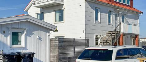 Een wit huis met twee verdiepingen, een rood dak, een balkon en een auto ervoor geparkeerd.