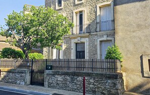 Un edificio de piedra con balcón y un árbol en primer plano.