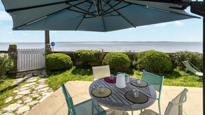 An outdoor patio with a table and chairs, a large umbrella, and a view of the sea. - Awesome home in Saint-Trojan-les-Bains (Saint-Trojan-les-Bains)