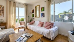 A spacious living room with a large white sofa, a wooden coffee table, and a view of the sea through large windows. - Awesome home in Saint-Trojan-les-Bains (Saint-Trojan-les-Bains)