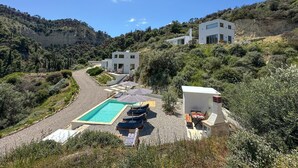 Una villa moderna con piscina, mobiliario exterior y vistas de las colinas circundantes.