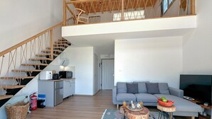 Amplia sala de estar con una escalera, un sofá, una mesa de centro y una televisión.