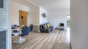 A modern living room with a dining area, a sofa, a TV, and a small table with a plant.