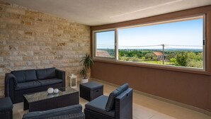 A balcony with wicker furniture, a stone wall, and a large window offering a view of a rural landscape. - Awesome apartment in Skabrnja (Skabrnja)