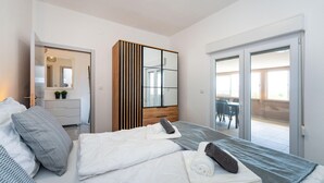 A modern hotel room with a bed, a wooden wardrobe, a mirror, and a sliding glass door leading to a balcony. - Awesome apartment in Skabrnja (Skabrnja)
