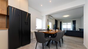 A modern kitchen with a black refrigerator, a dining area with a wooden table and grey chairs, and a living area with a dark sofa and a TV. - Awesome apartment in Skabrnja (Skabrnja)