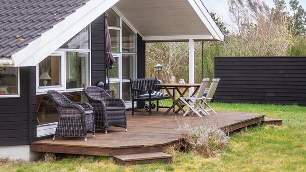 A house with a wooden deck, outdoor seating, and a large window overlooking the yard.