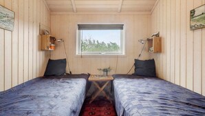 A small cabin with two single beds, a window with a view of trees, and wooden walls.