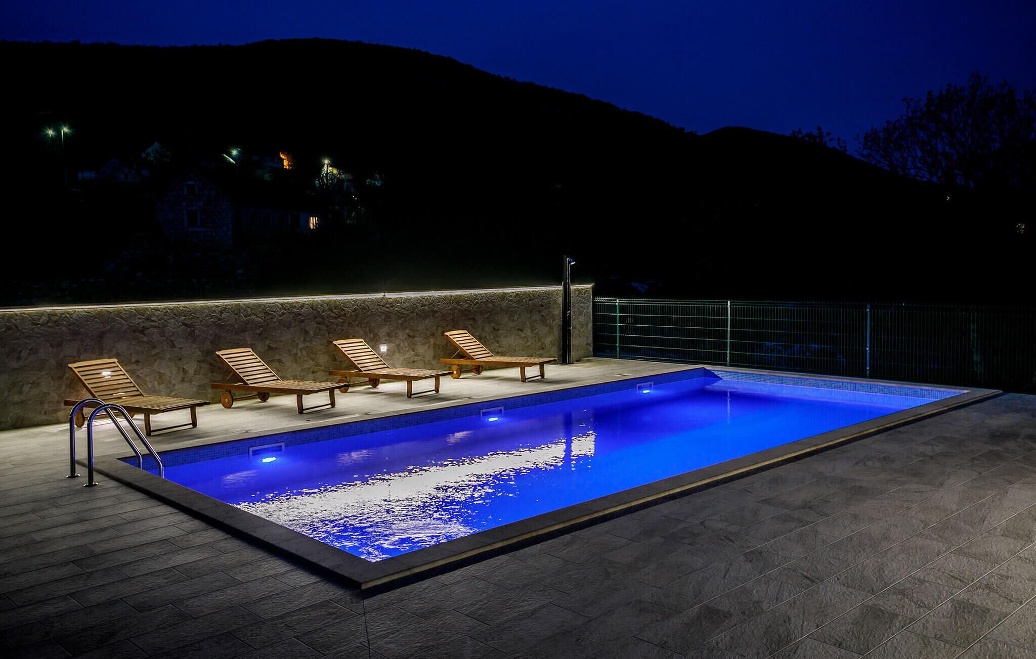 Ein Swimmingpool mit vier Holzliegen und einer Steinmauer.