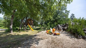 Un terrain de jeux avec un toboggan et des structures d’escalade, entouré d’arbres et de rochers.