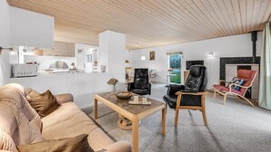 A modern living room with a sofa, coffee table, and two leather chairs. A kitchen with white cabinets and a dining area with a table and chairs are visible in the background. - 2 bedroom beautiful home in Tarm (Tarm)