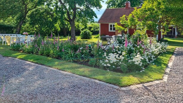 A house with a red exterior, surrounded by a well-maintained garden with various flowers and a gravel driveway.