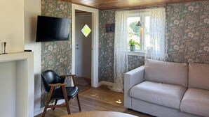 A living room with a wooden ceiling, floral wallpaper, a television mounted on the wall, a sofa, and a chair.