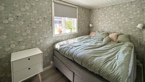 A bedroom with a bed, a nightstand, a window, and a lamp.