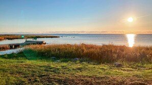 A coastal landscape with a clear sky, a body of water, and a grassy area with rocks.