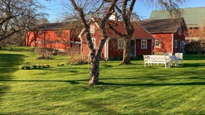A red wooden house with a sloped roof, surrounded by a well-maintained lawn and a few trees.