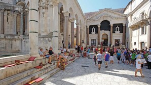 Una plaza histórica con arquitectura clásica, incluyendo columnas y arcos, y una multitud de gente.