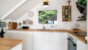 A modern kitchen with a wooden countertop, a built-in oven, and a window with a view of greenery.